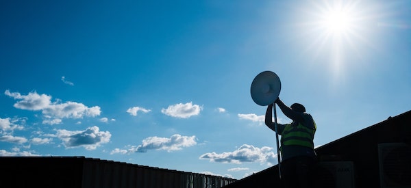 a man holding hands up while installing an antenna against sun