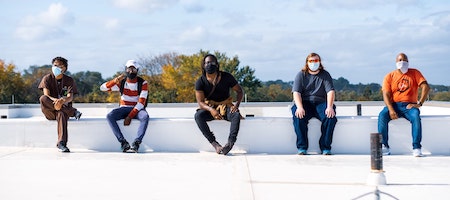 five men with face masks sitting on the wall