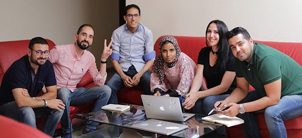 six people sitting on the couch with laptop in front of them on the table