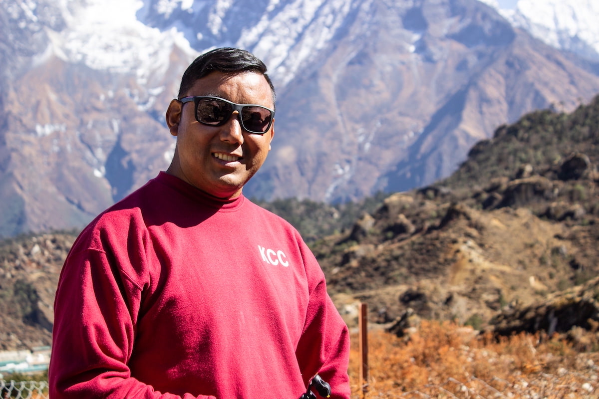 a stunning mountainous landscape, with snow-capped peaks and a man smiling at the camera