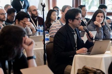 People at NDSS symposium listening while one man is talking with a microphone