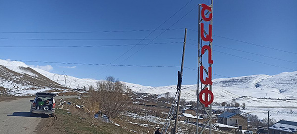 Snowcapped landscape and a road with car parked. To the right, a person installing an antenna.