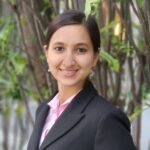 a young woman dressed in a business suit poses for a photo, standing in front of a tall tree