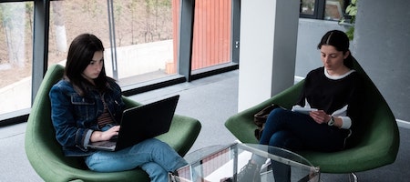 two girls sitting looking at laptop screens